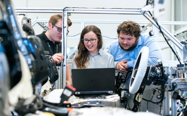 Eine Frau und zwei Männer vor einem Laptop, die darüber nachdenken, wie die Produktivität in der Fertigung verbessert werden kann. / A woman and two men in front of a laptop contemplating how to improve productivity in manufacturing.