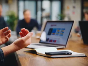 A person gesturing during a meeting, with a laptop and notebook on the table; symbolizing open communication when managing resistance in teams.