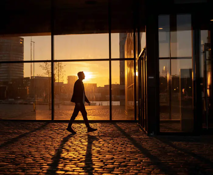 Eine Person läuft im Gegenlicht auf eine Glasfassade zu, in der sich ihr Schatten spiegelt – Symbol für den Wiedereinstieg ins Unternehmen und einen neuen beruflichen Abschnitt.