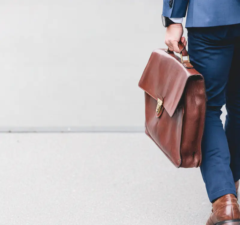 A person in a suit walks away with a leather briefcase – symbolizing professional transition and the deliberate preparation for an exit.